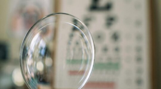 Close-up macro shot of prescription chart with eyeglass lens in foreground creating refraction effect